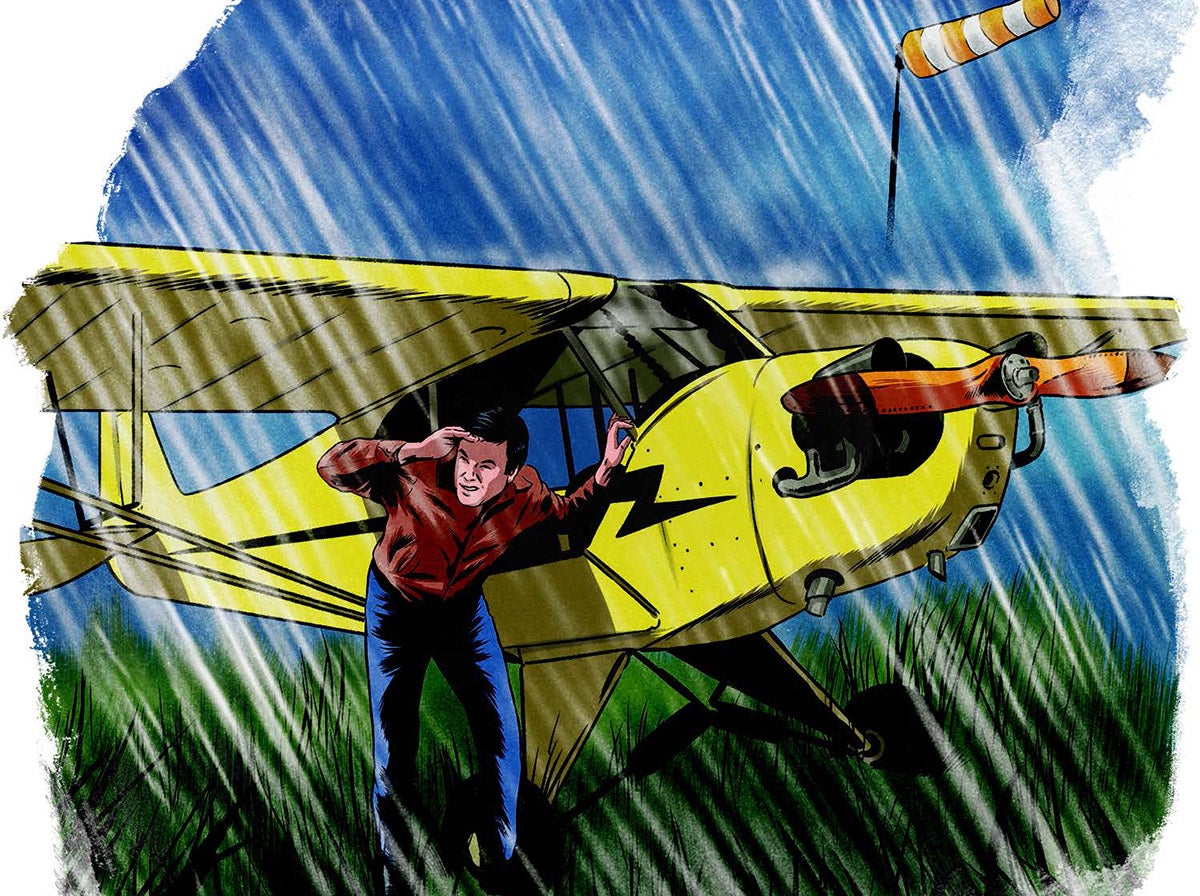 A man takes cover under the wing of his aircraft during a rainstorm.