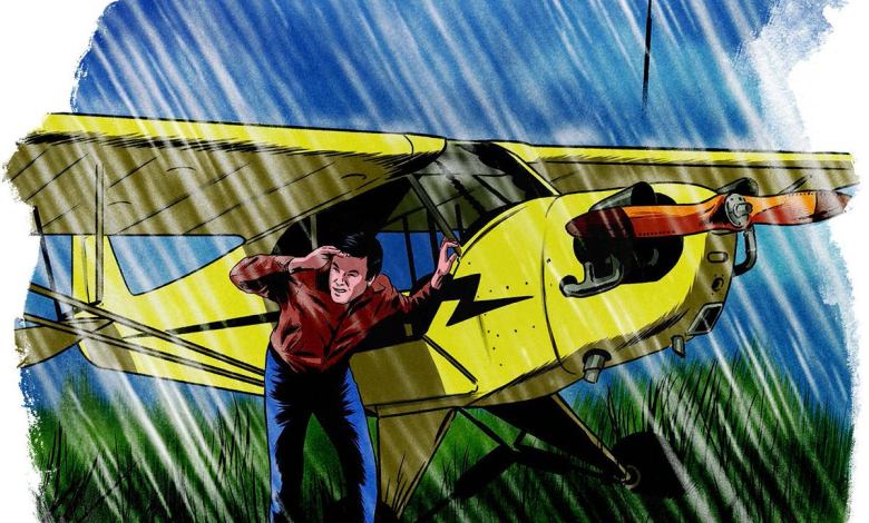A man takes cover under the wing of his aircraft during a rainstorm.