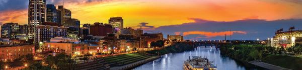 The city of Nashville at sunset. A paddle wheel cruise ship cruises down the Cumberland River amid a backdrop of the downtown area.