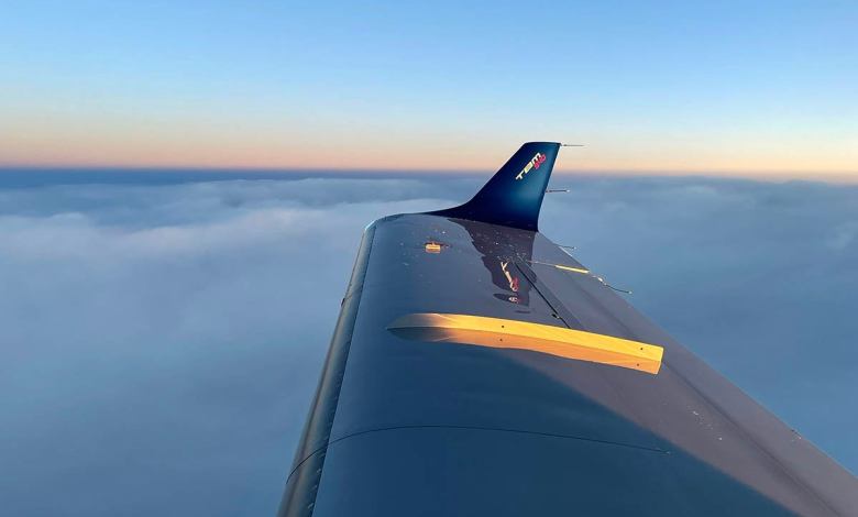 The wing and wingtip of a TBM 940 aircraft with a bed of clouds below and the horizon in the distance