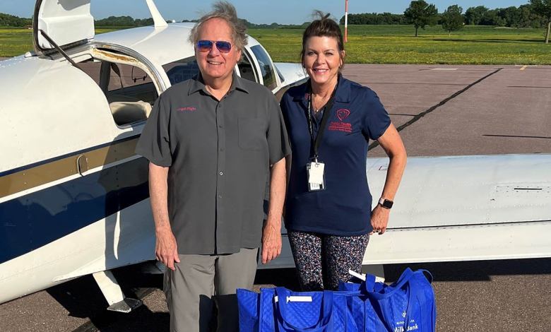 Two people stand in front of a Mooney aircraft on a tarmac with bags of breast milk to be delivered to medically fragile babies.