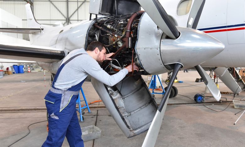 Aircraft mechanic repairs an engine in an airport hangar. [Shutterstock]