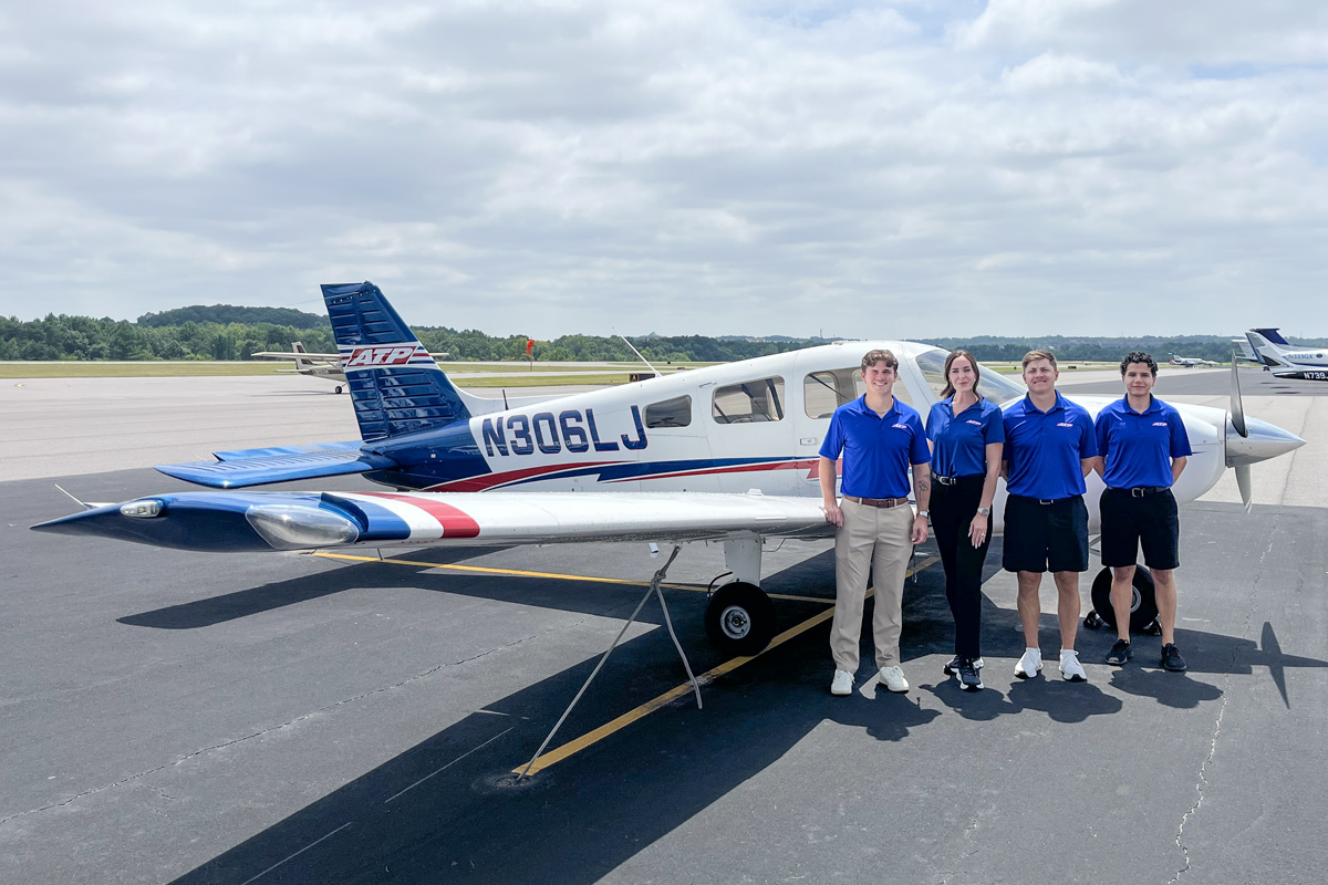 ATP Flight School students standing beside a Piper Archer training aircraft on the tarmac, wearing blue ATP uniforms, preparing for pilot training.