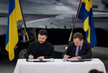 Sweden Prime Minister Alf Kristersson and Ukraine President Volodymyr Zelenskyy sign a purchase agreement behind a desk.