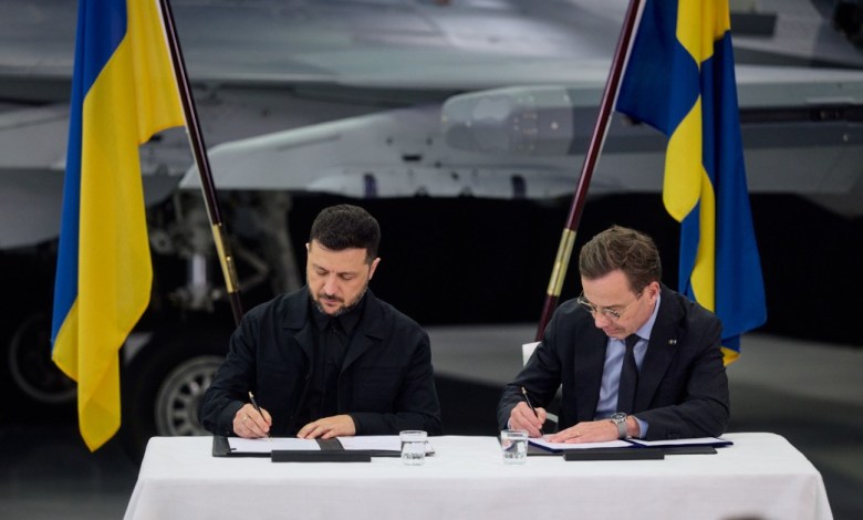 Sweden Prime Minister Alf Kristersson and Ukraine President Volodymyr Zelenskyy sign a purchase agreement behind a desk.