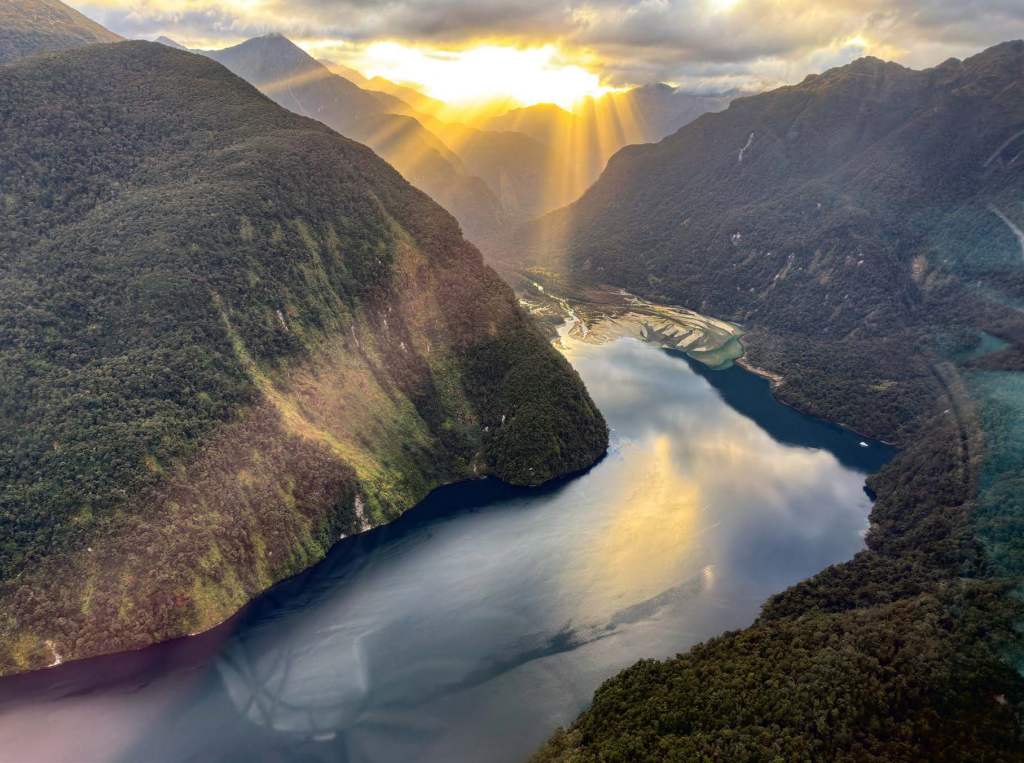 The sun cascades over the jagged peaks surrounding one of New Zealand’s many fiords. [Credit: Max Trescott]
