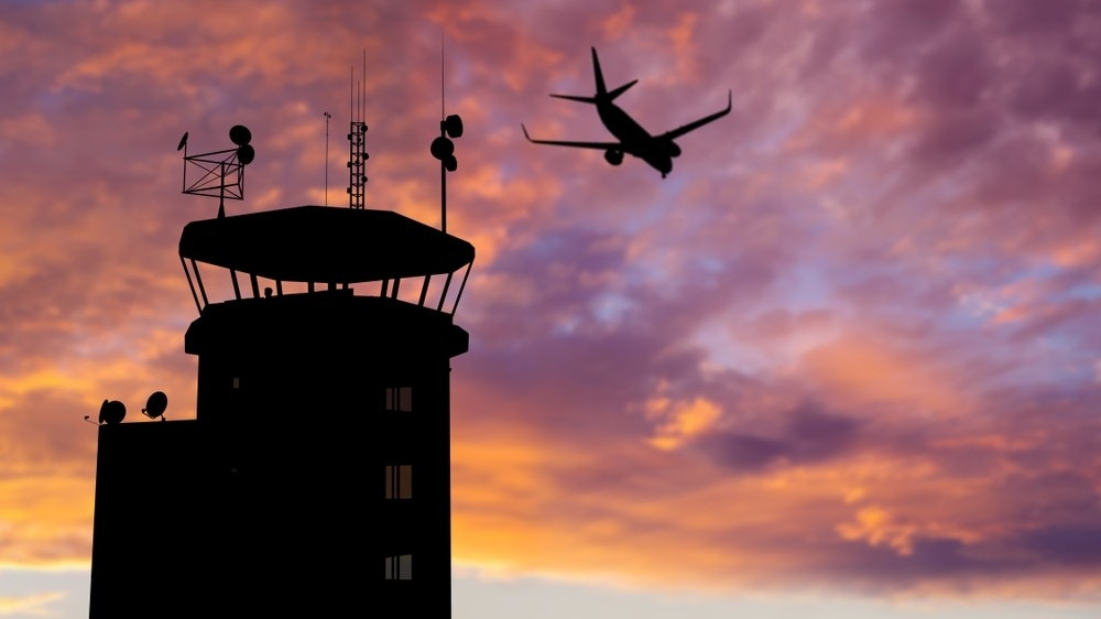 Silhouette of air traffic control (ATC) tower during sunset with airplane flying overhead