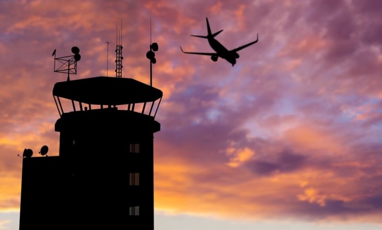 Silhouette of air traffic control (ATC) tower during sunset with airplane flying overhead