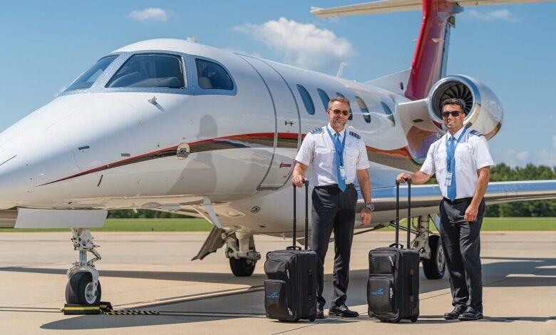 Two private pilots stand on the ramp in front of a private jet with suitcases in hand.